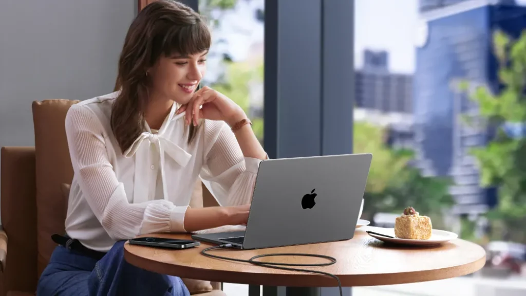 Γυναίκα σε καφέ δουλεύει σε MacBook που φορτίζει με καλώδιο USB-C UGREEN